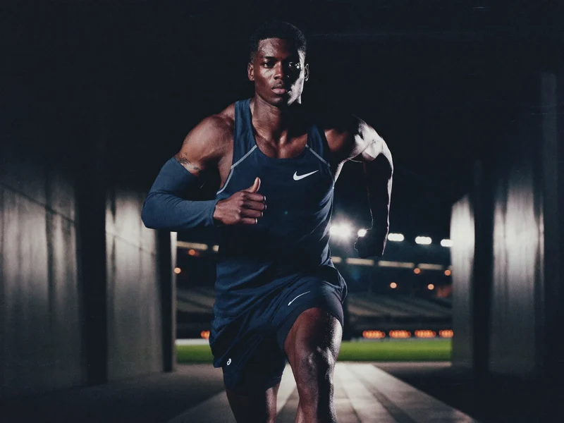 Sprinter in dunkler Performance-Kleidung im beleuchteten Stadiontunnel bei Nacht
