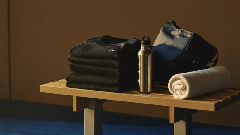 Umkleidebank mit Sporttasche, gefalteter dunkler Sportkleidung, Flasche und Handtuch